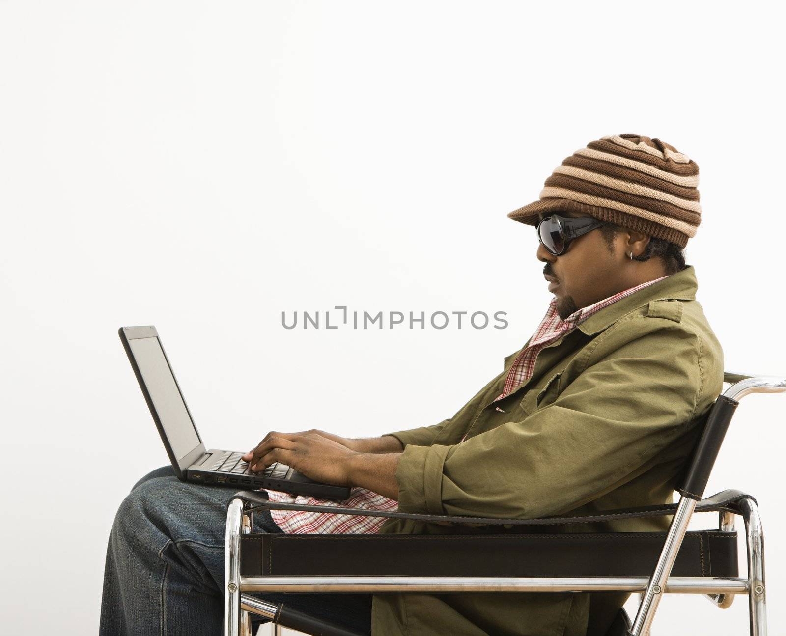 Side view of African-American mid-adult man wearing hat and typing on laptop computer.