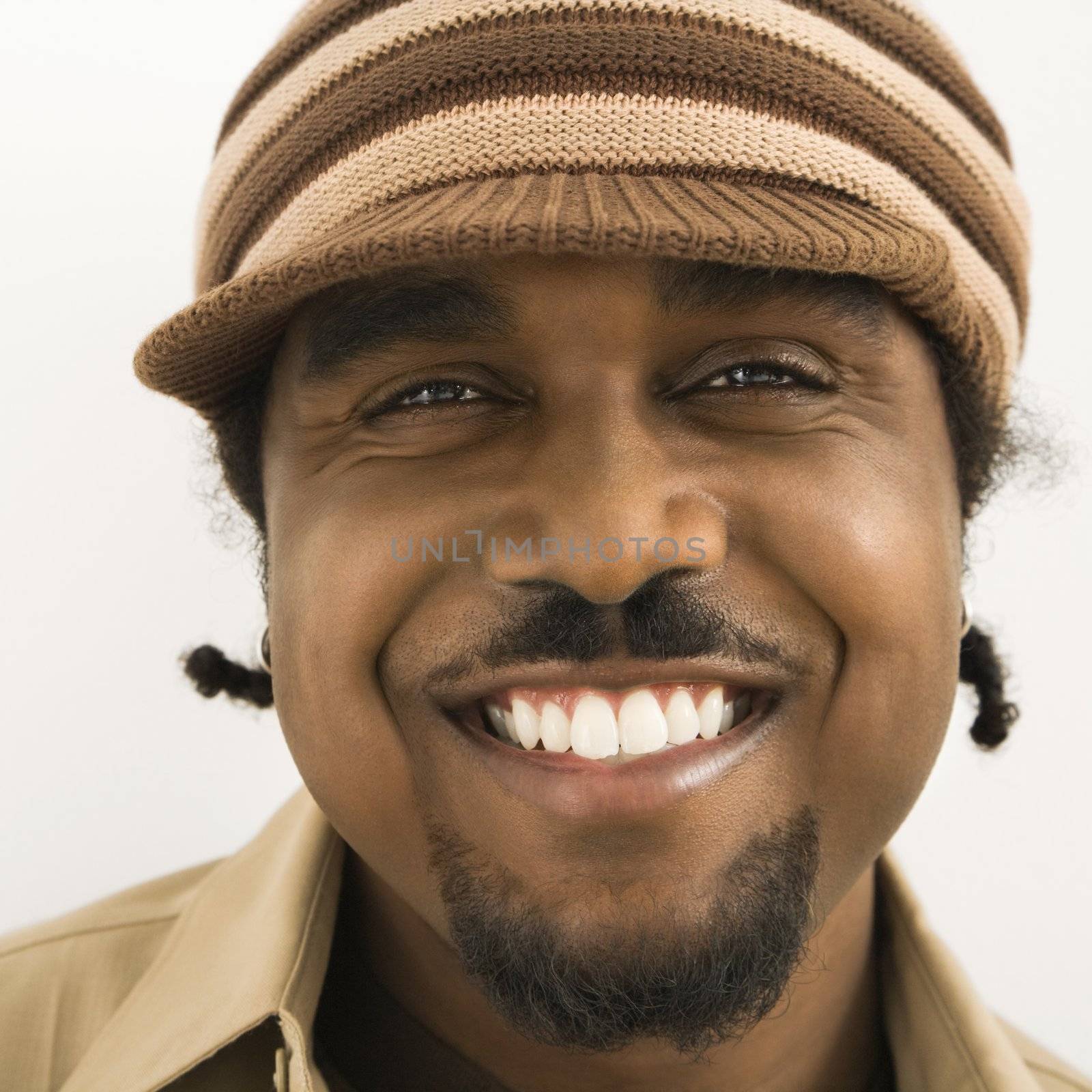 Close up of African-American mid-adult man wearing knit hat with brim smiling at viewer.