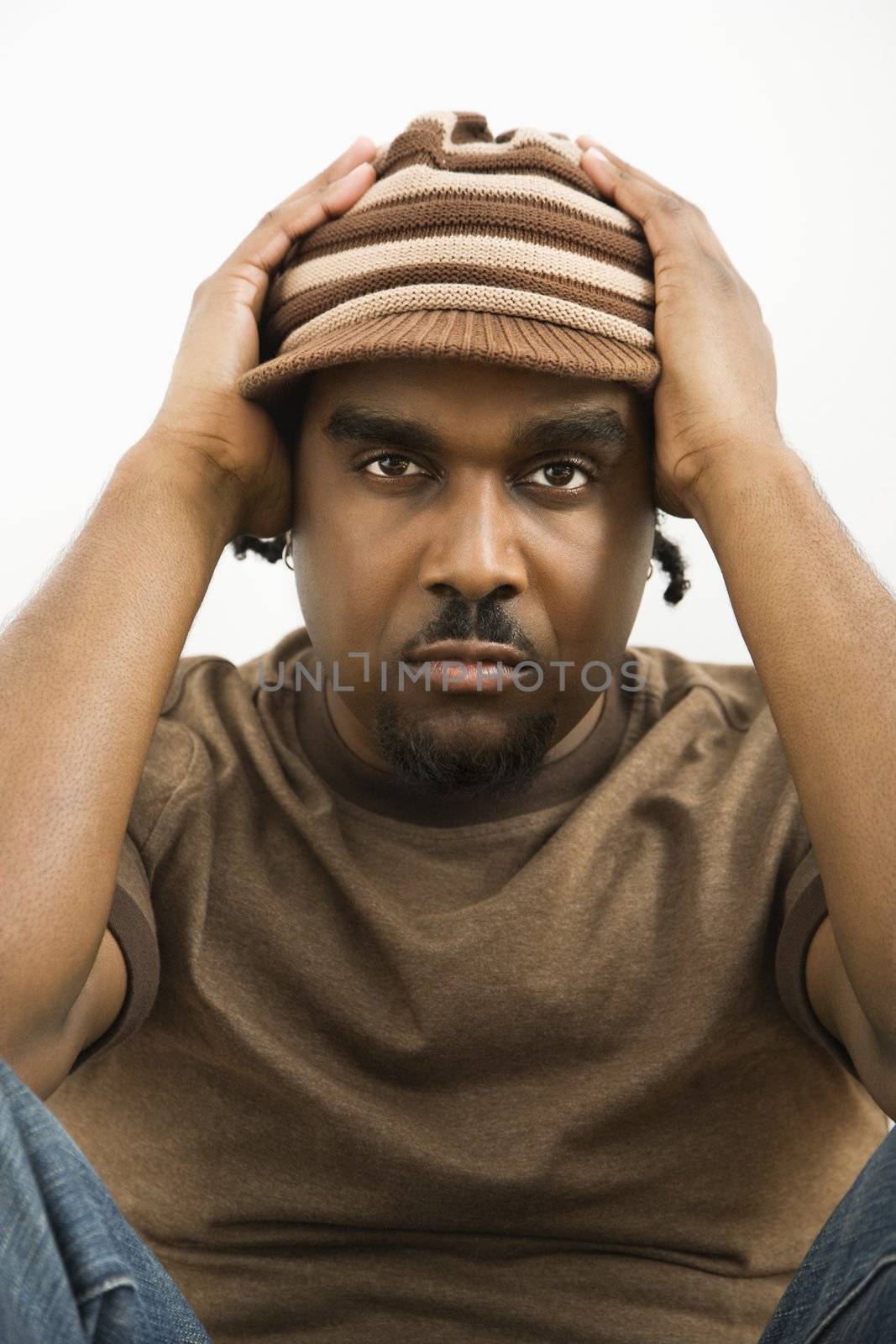 African-American mid-adult man holding head wearing hat looking at viewer.