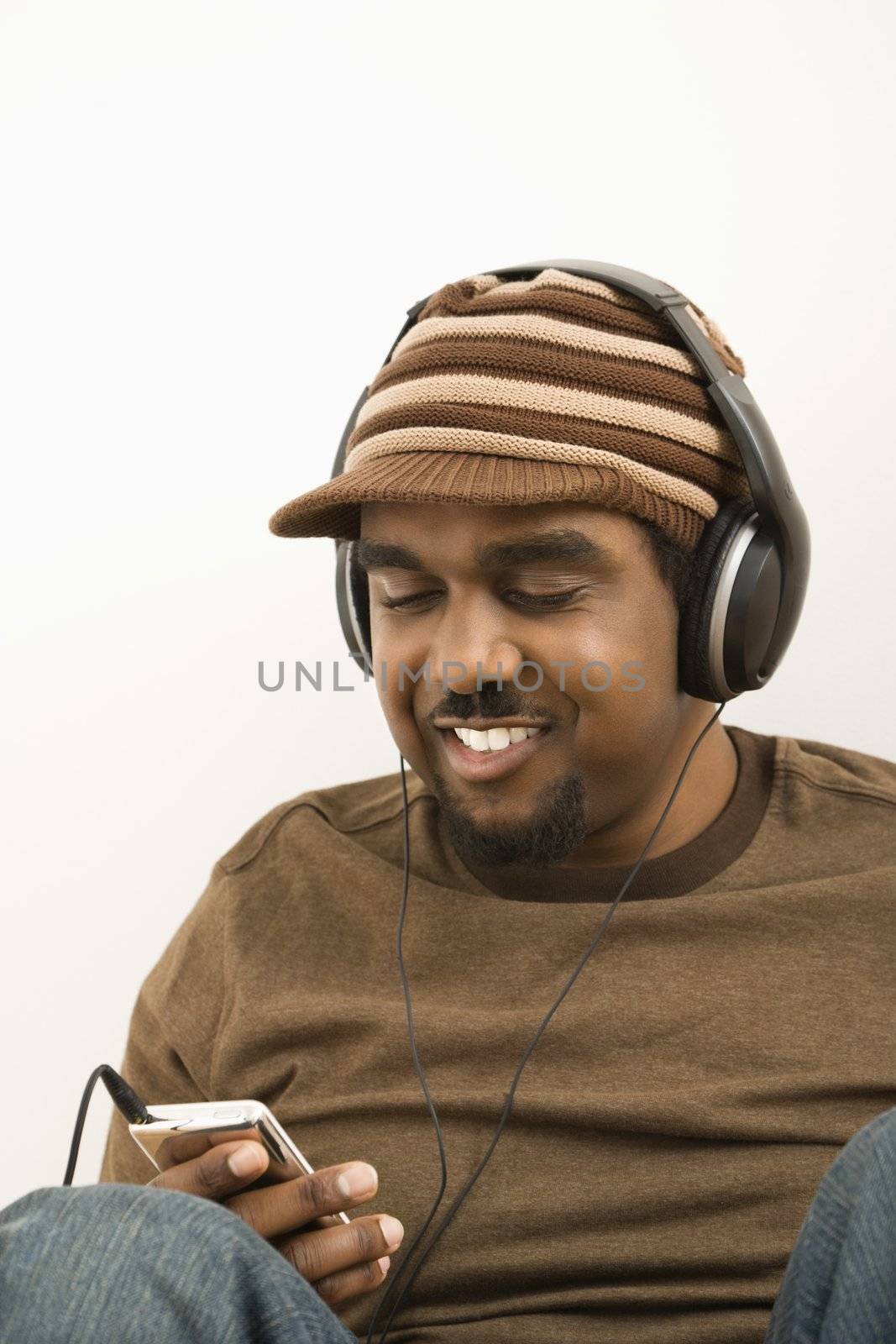 African-American mid-adult man wearing hat and listening to mp3 player.