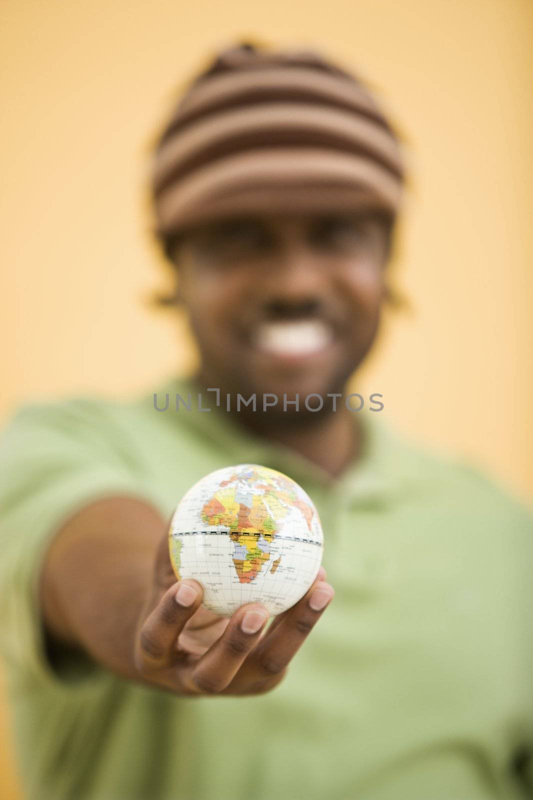 African-American mid-adult man wearing hat holding small globe to viewer.