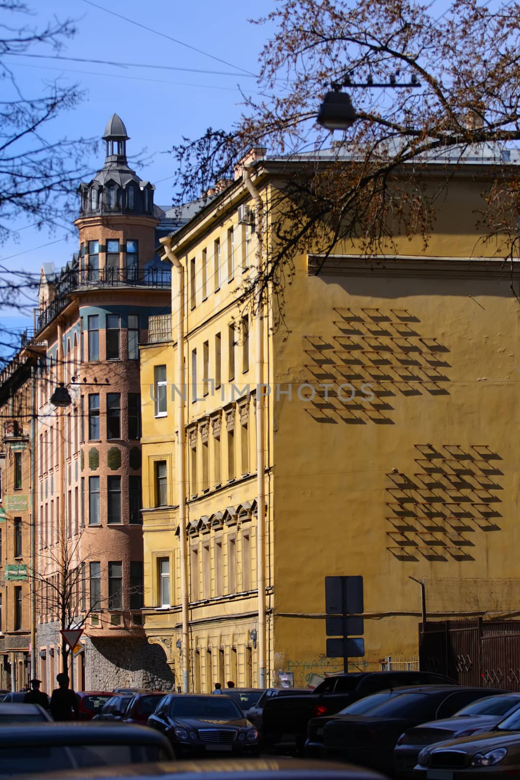 Center of city. Old houses, cars and wall of old house with strange iron construction which cast strict geometrical shadows.
