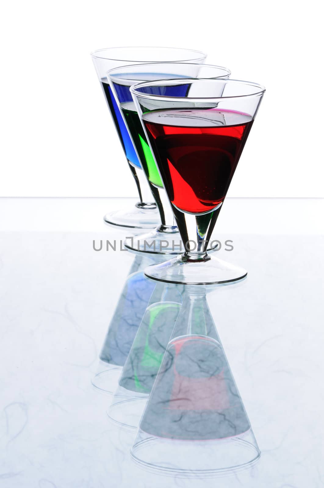 Three transparent glasses with multi-coloured drinks
