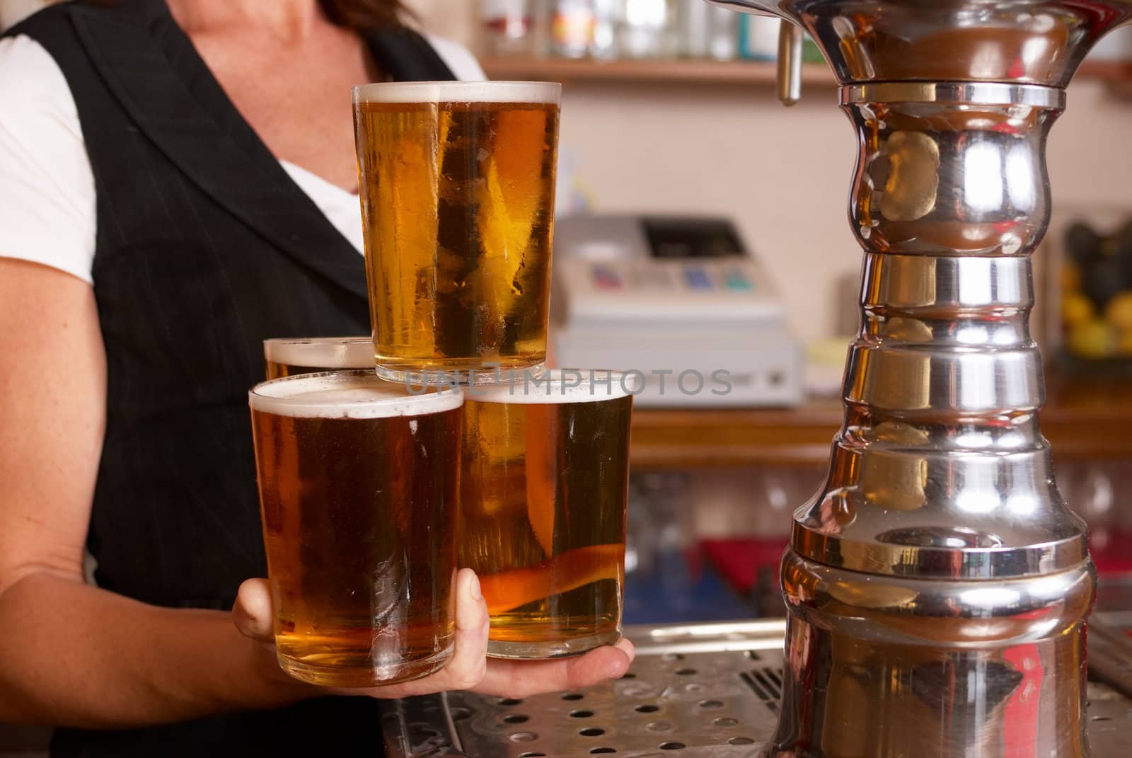 Skilful waitress holding four freshly filled pint glasses in one hand