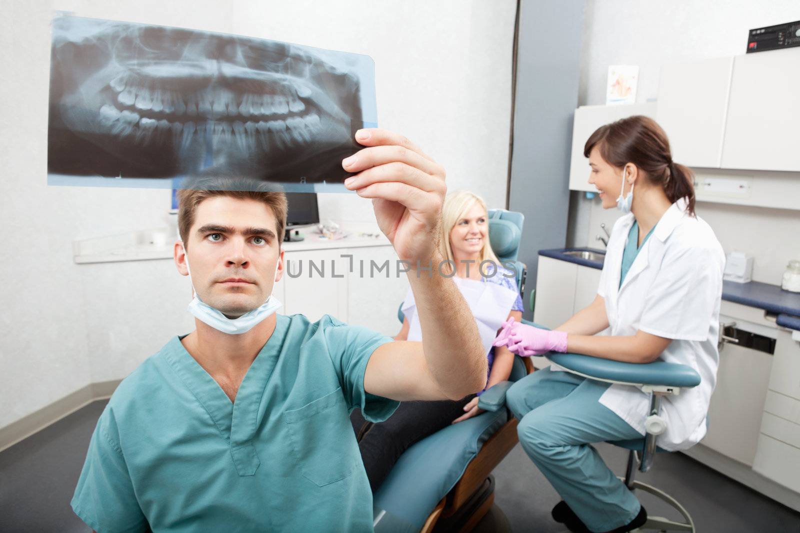 Radiodentist checking x-ray with assistant and patient having conversation in the background