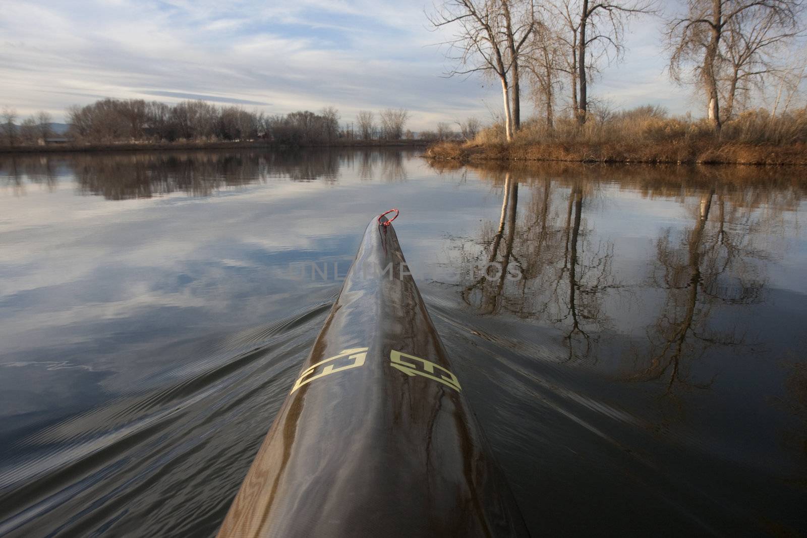 bow of racing kayak with wake on a calm lake, water reflections, , late autumn or early spring, thirteen - temporary race number placed on deck by myself