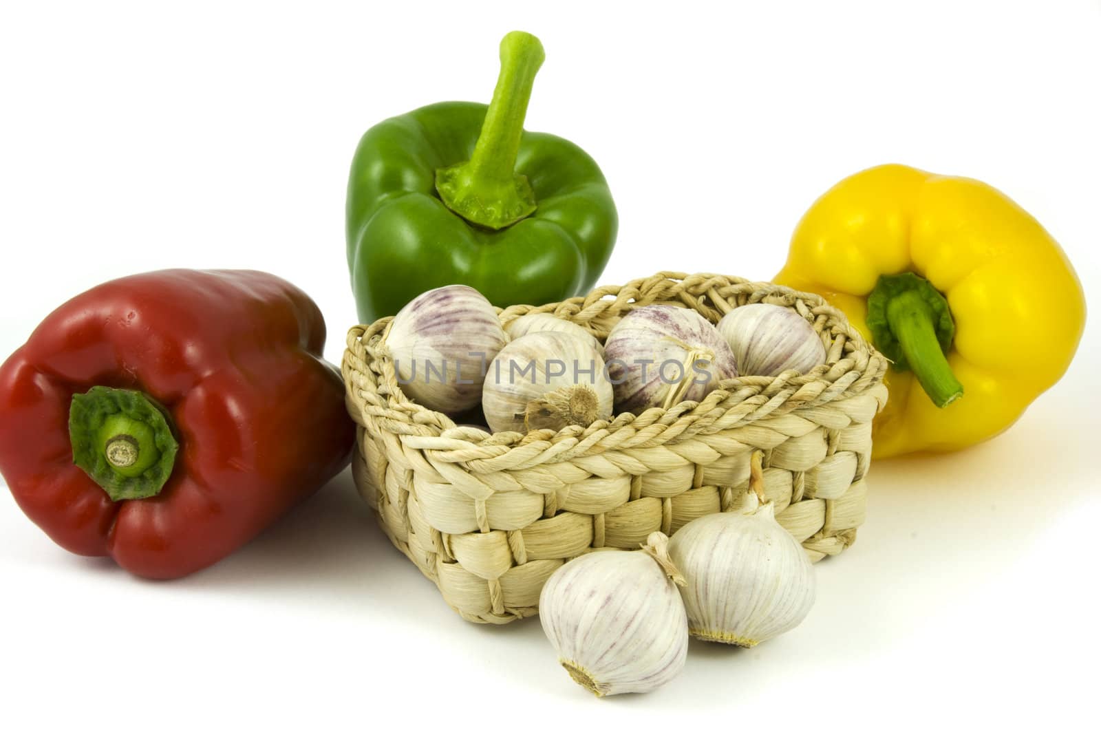 Three bell peppers and basket full of fresh garlics isolated on white background