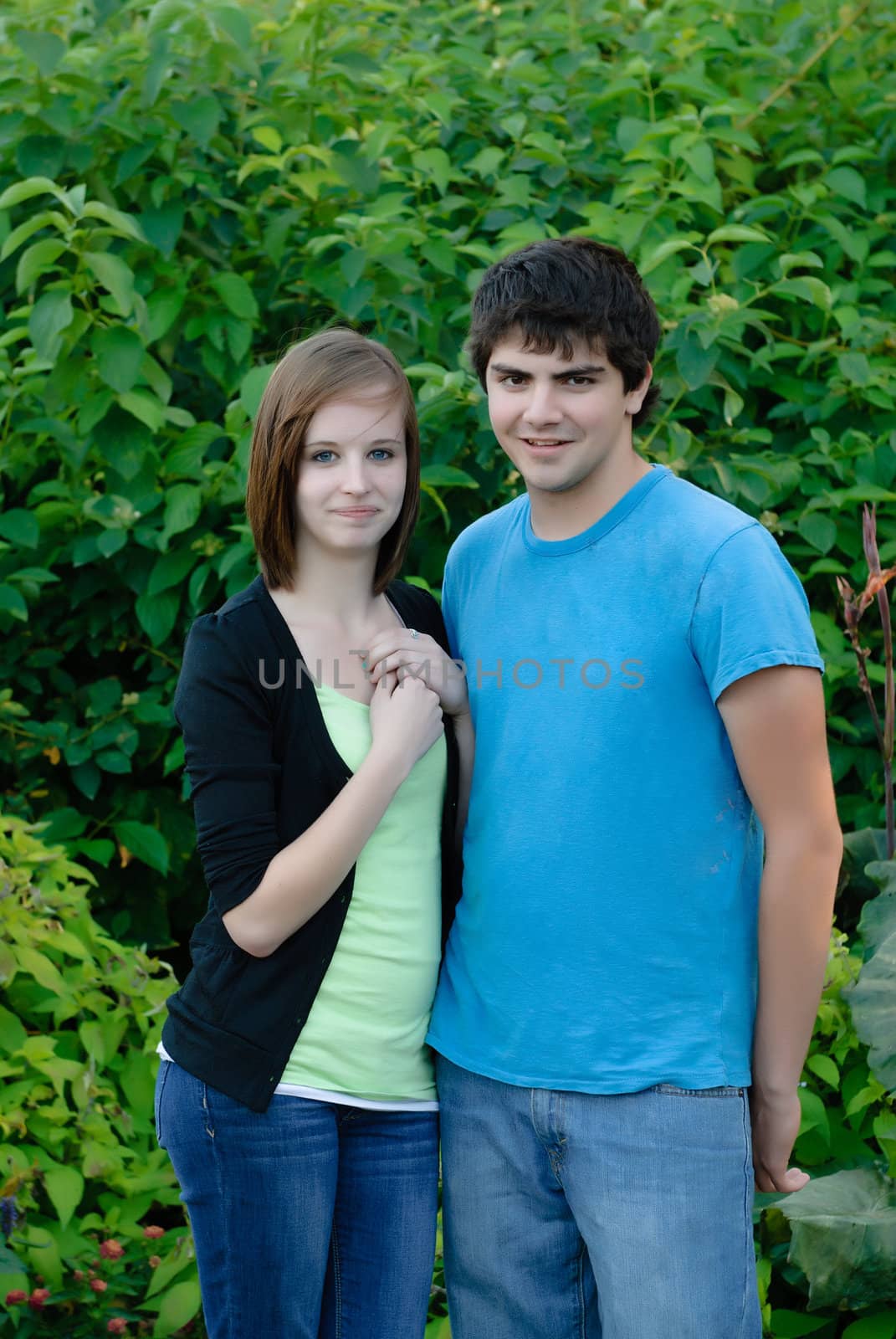 A young couple standing next to each other with green leaves in the background.
