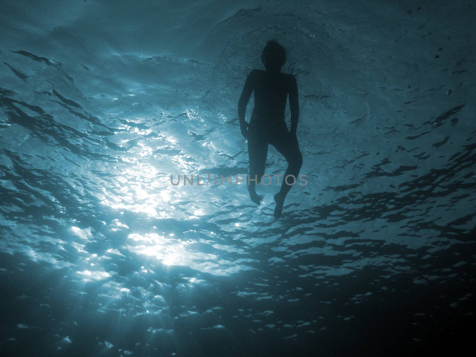 Child, in back-light, swim in the sea.