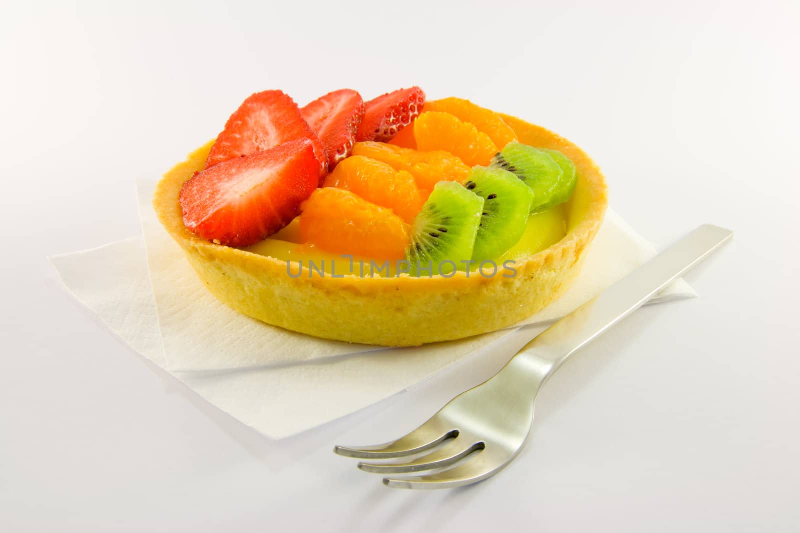 Strawberry, mandarin and kiwi custard fruit tart on a napkin with fork on a  white background