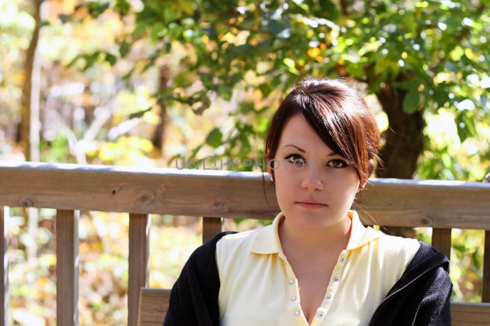 Attractive young woman sitting on a bench outdoors on a beautiful autumn day looking into the camera.