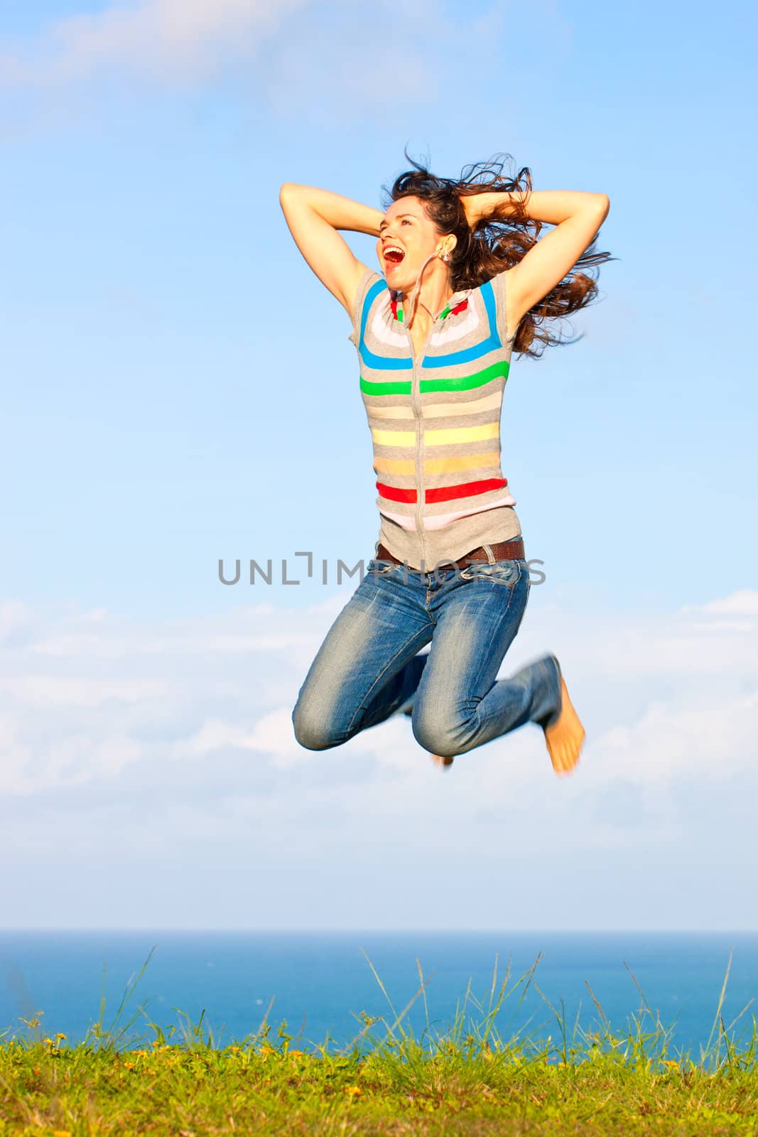 Beautiful young woman jumping up in the air laughing and holding her hair in front a of a great ocean view