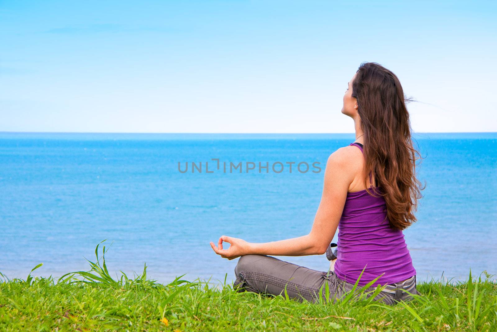 A beautiful young woman sitting meditating with a view of the ocean