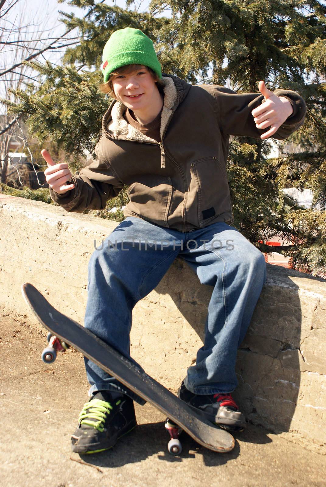 A young skateboarder poses outside on a concrete ledge.