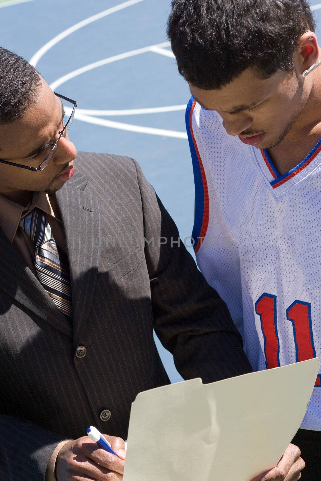 A basketball coach in a business suit sharing a play with a player on the team.   He could be also be recruiter trying to get him to sign a contract.