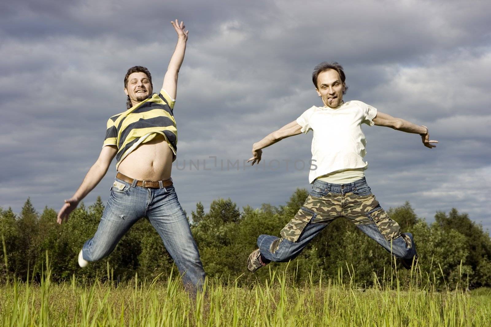Two young men joyfully jump on a grass