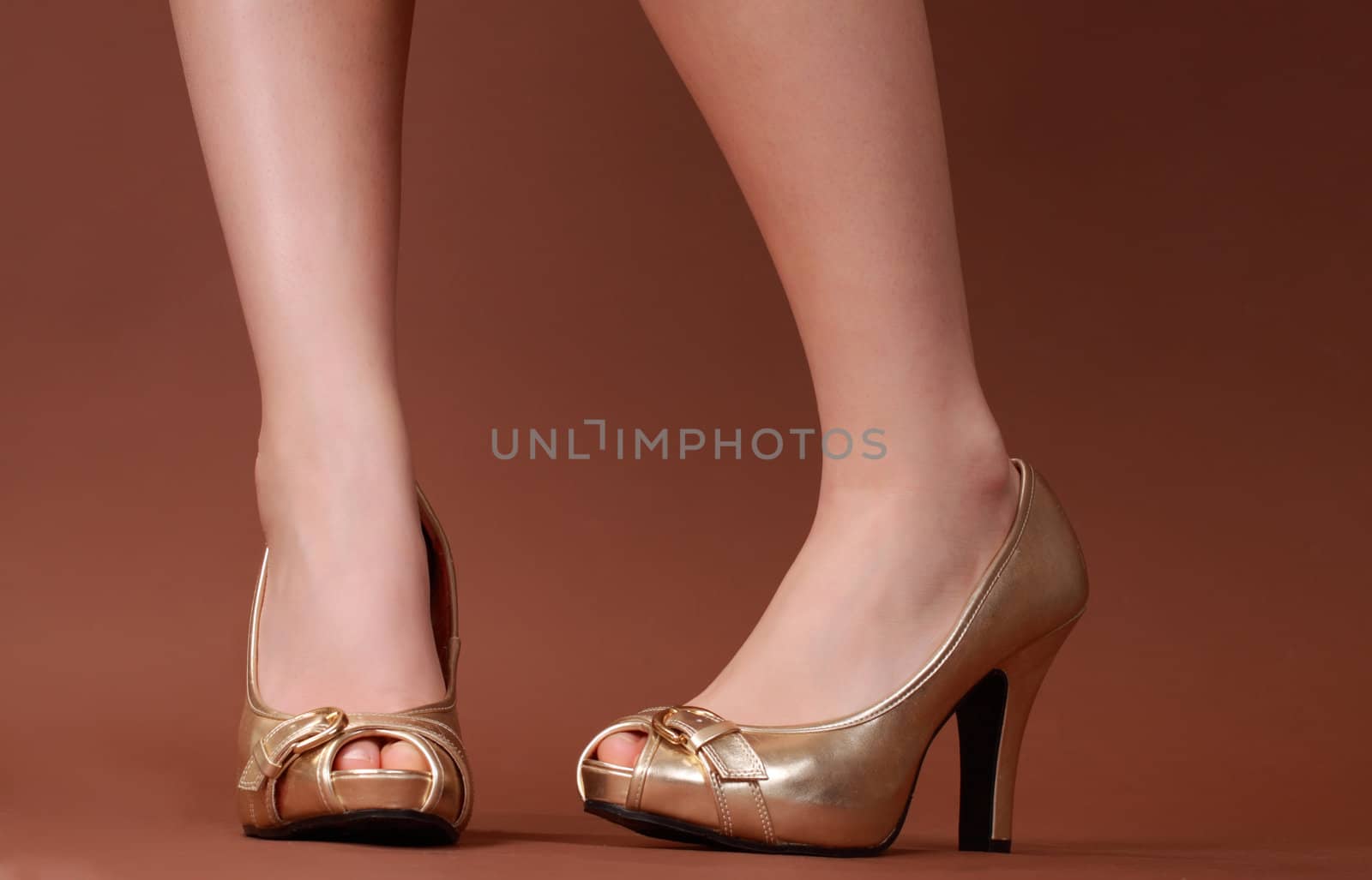 closeup on woman feet wearing gold shoes, brown background