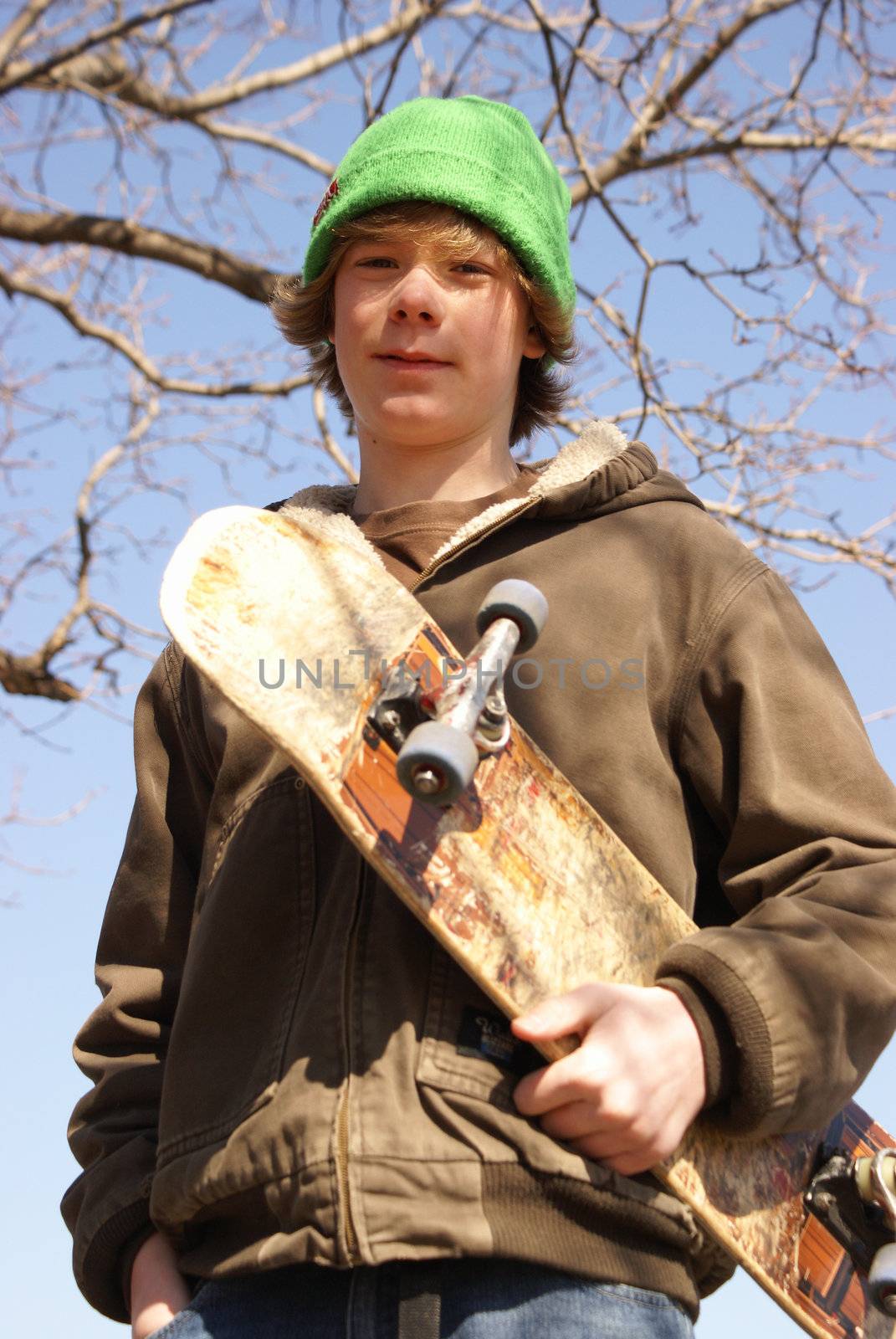 A young teen boy poses with his skateboard.