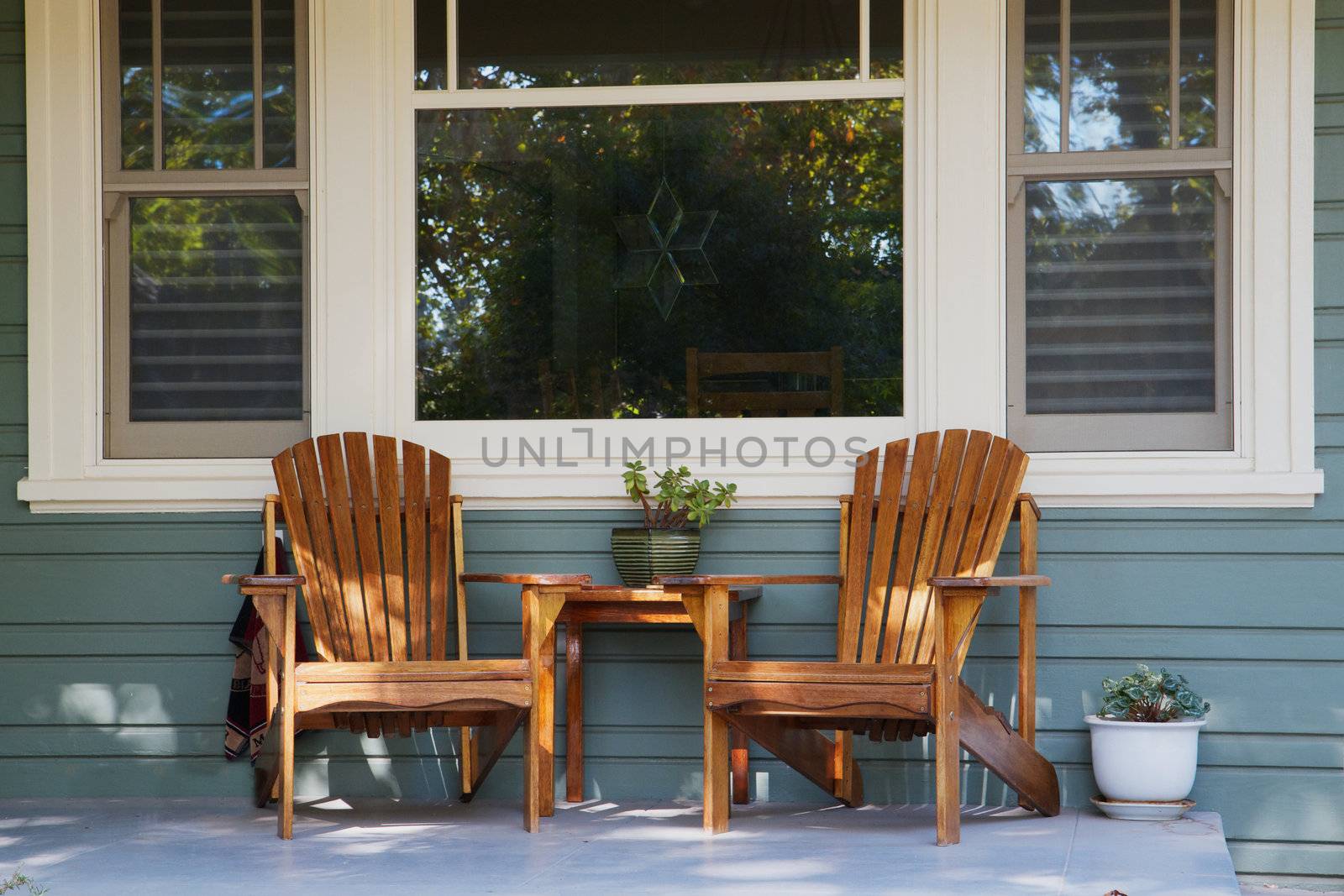 Two adirondack chairs on a porch with picture window background