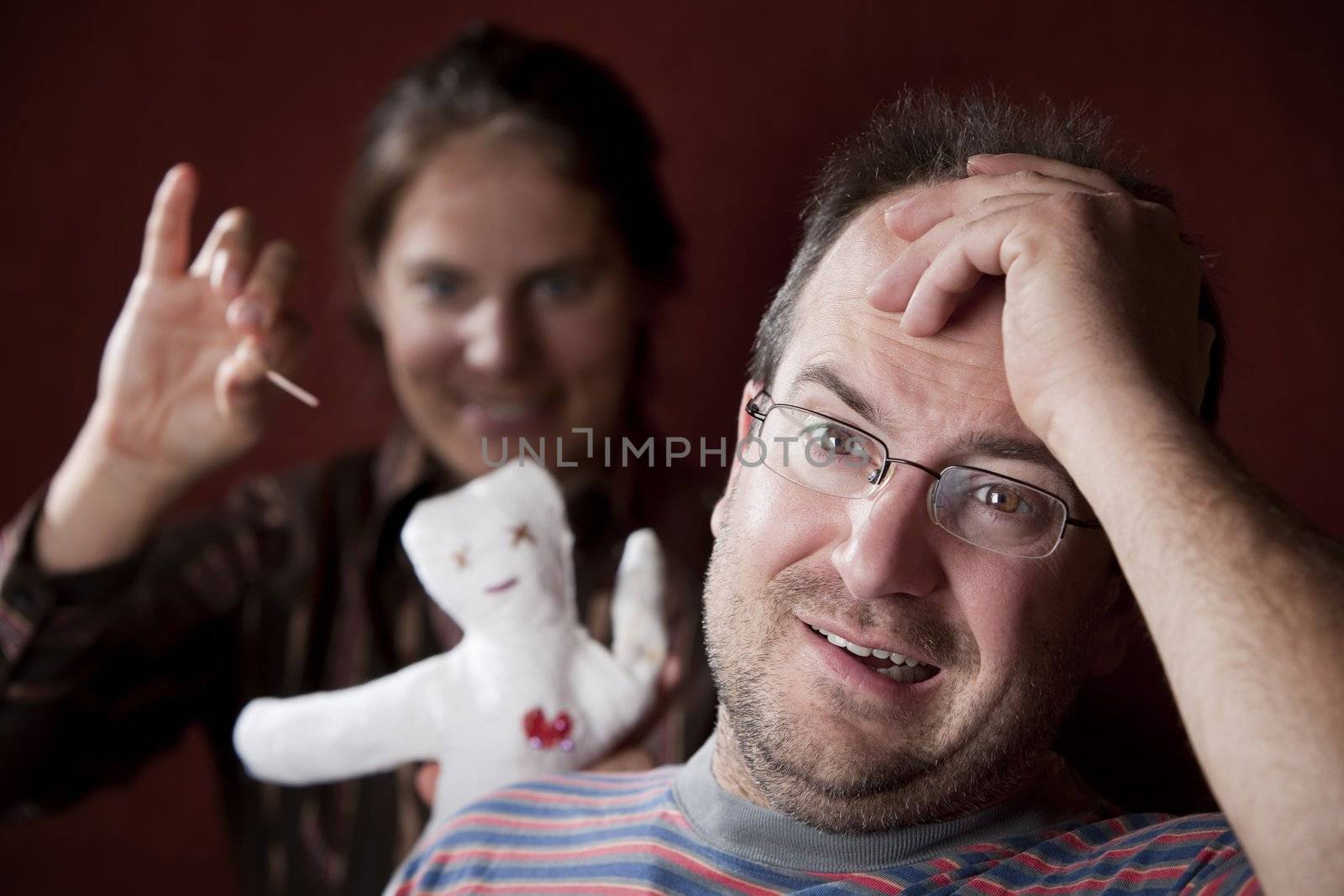 Guilty man with upset woman poking voodoo doll in the background