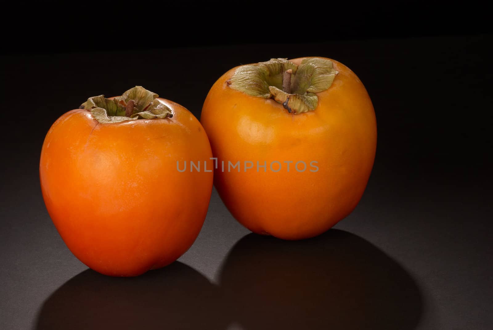 Two fresh ripe persimmons on black background