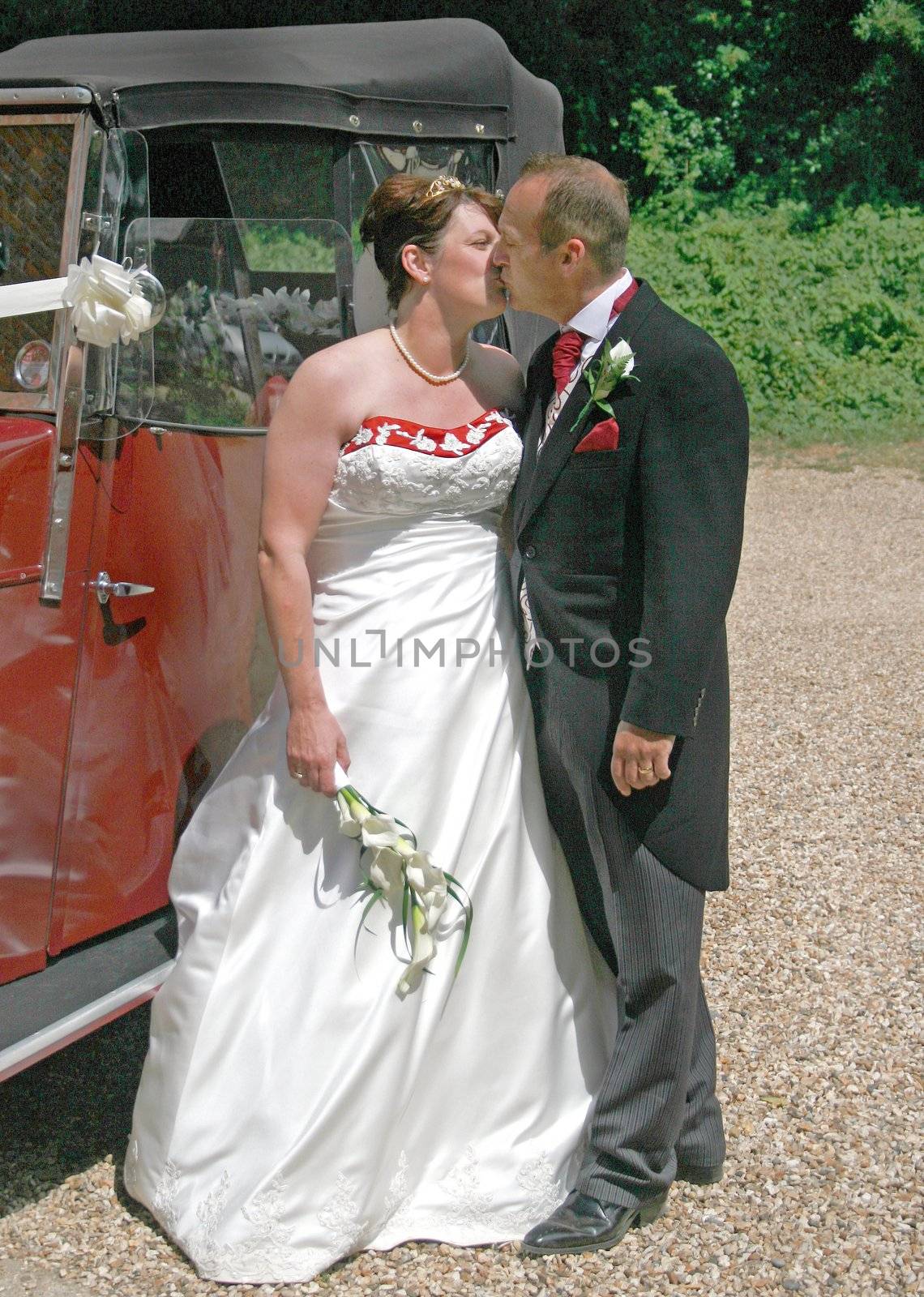 Bride and Groom Kissing in front of their Wedding Car