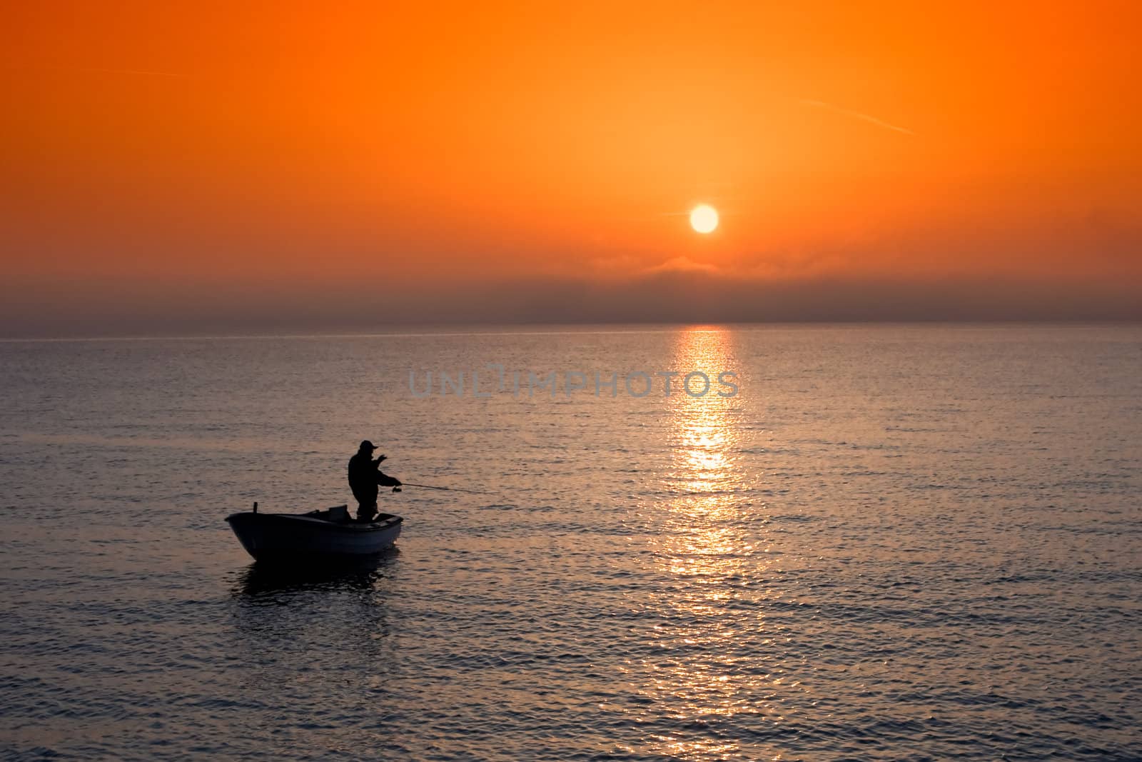 Man in a boat angling at sunset