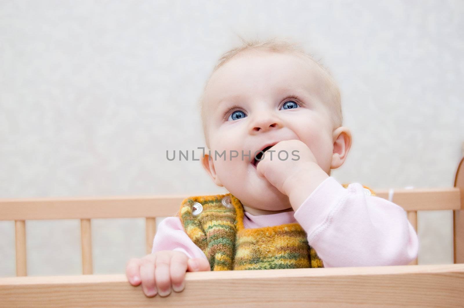 Curious baby with finger in mouth standing in bed