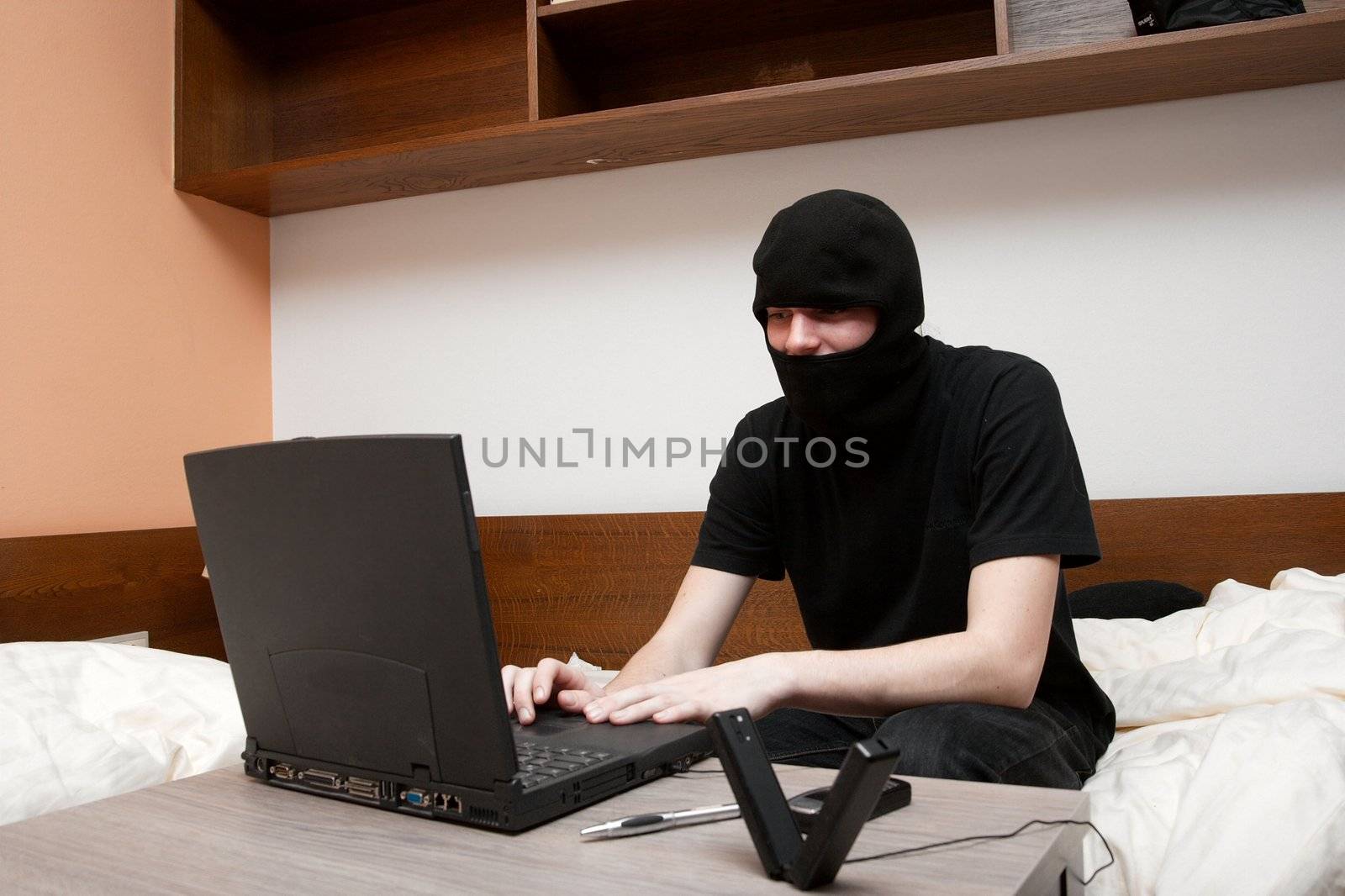 Black masked figure typing on a laptop