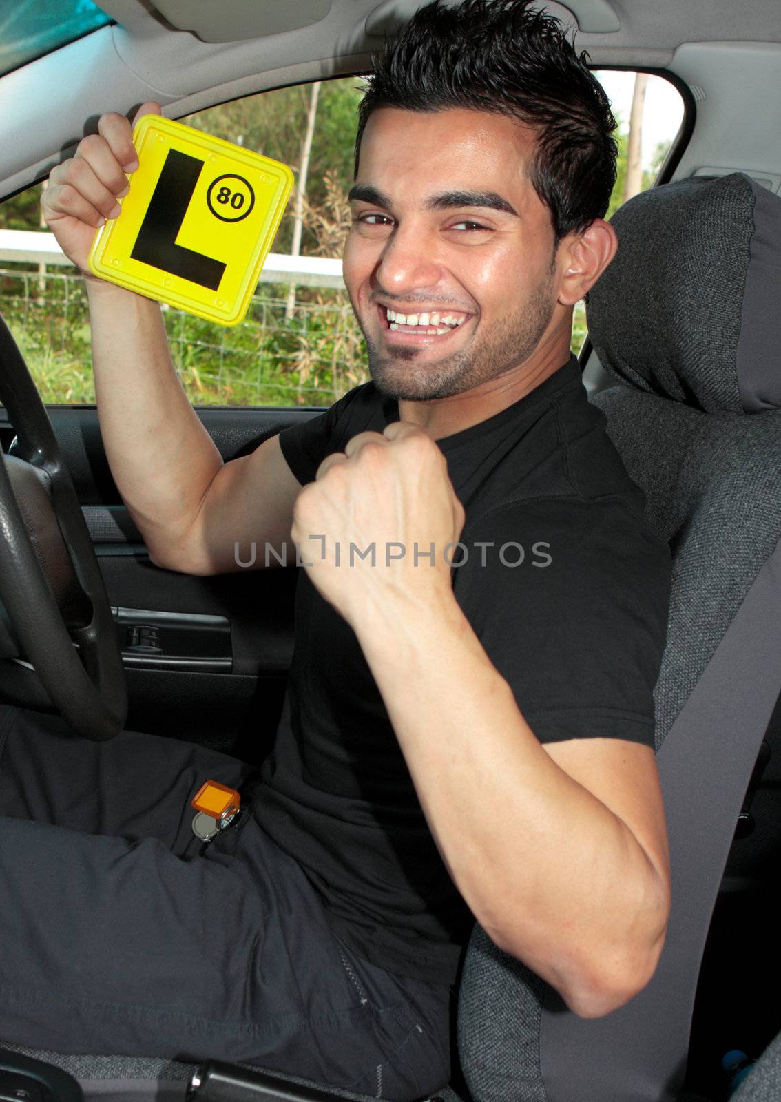 Happy male driver holding L learner plates and sitting in a car.