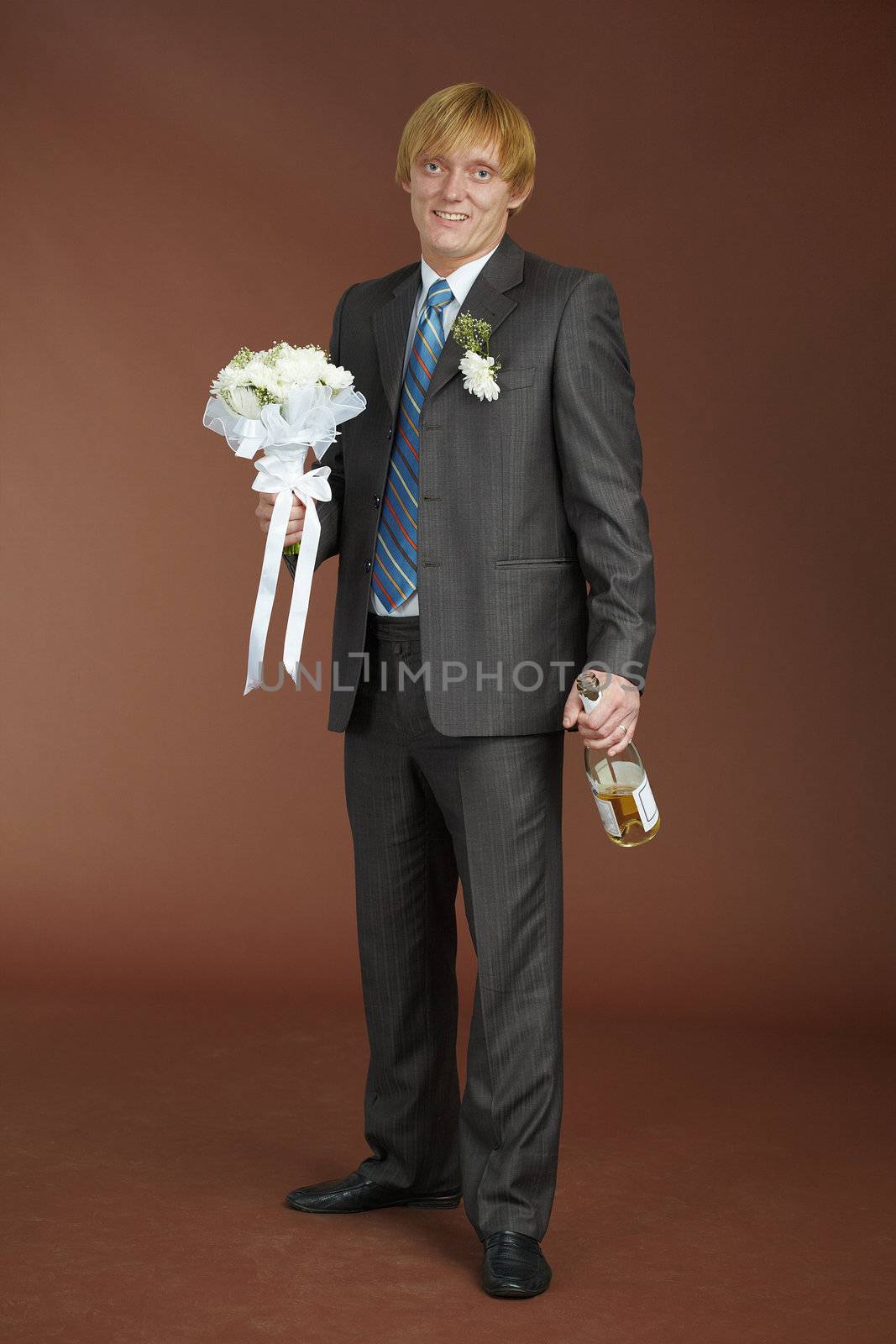 A young groom with a bouquet and a bottle of sparkling wine