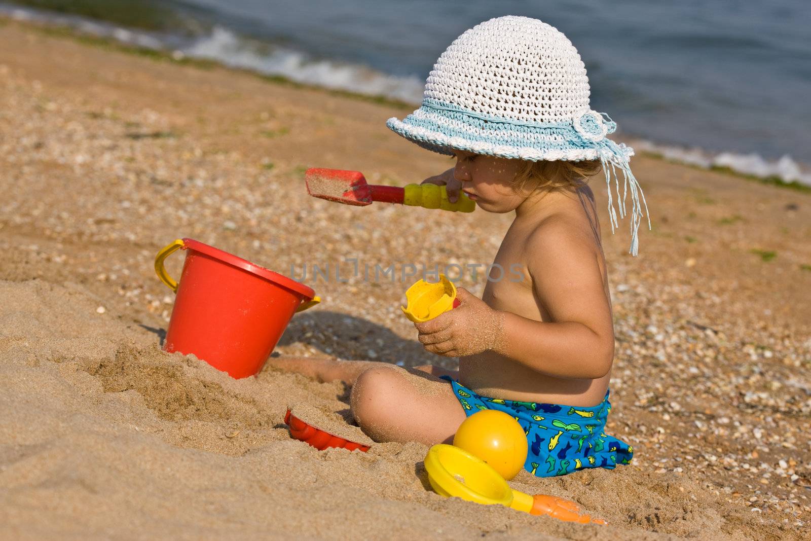 little girl in the bonnet plaing with sand,