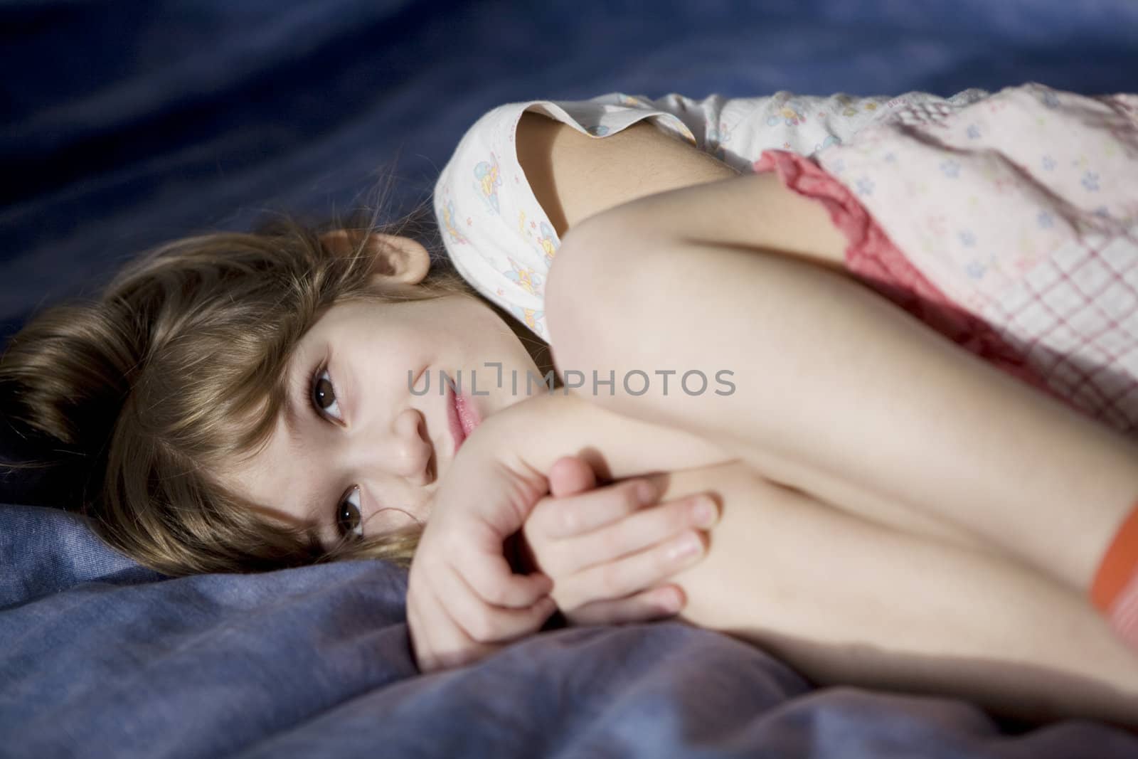 Little sad girl lying in bed. by elenarostunova