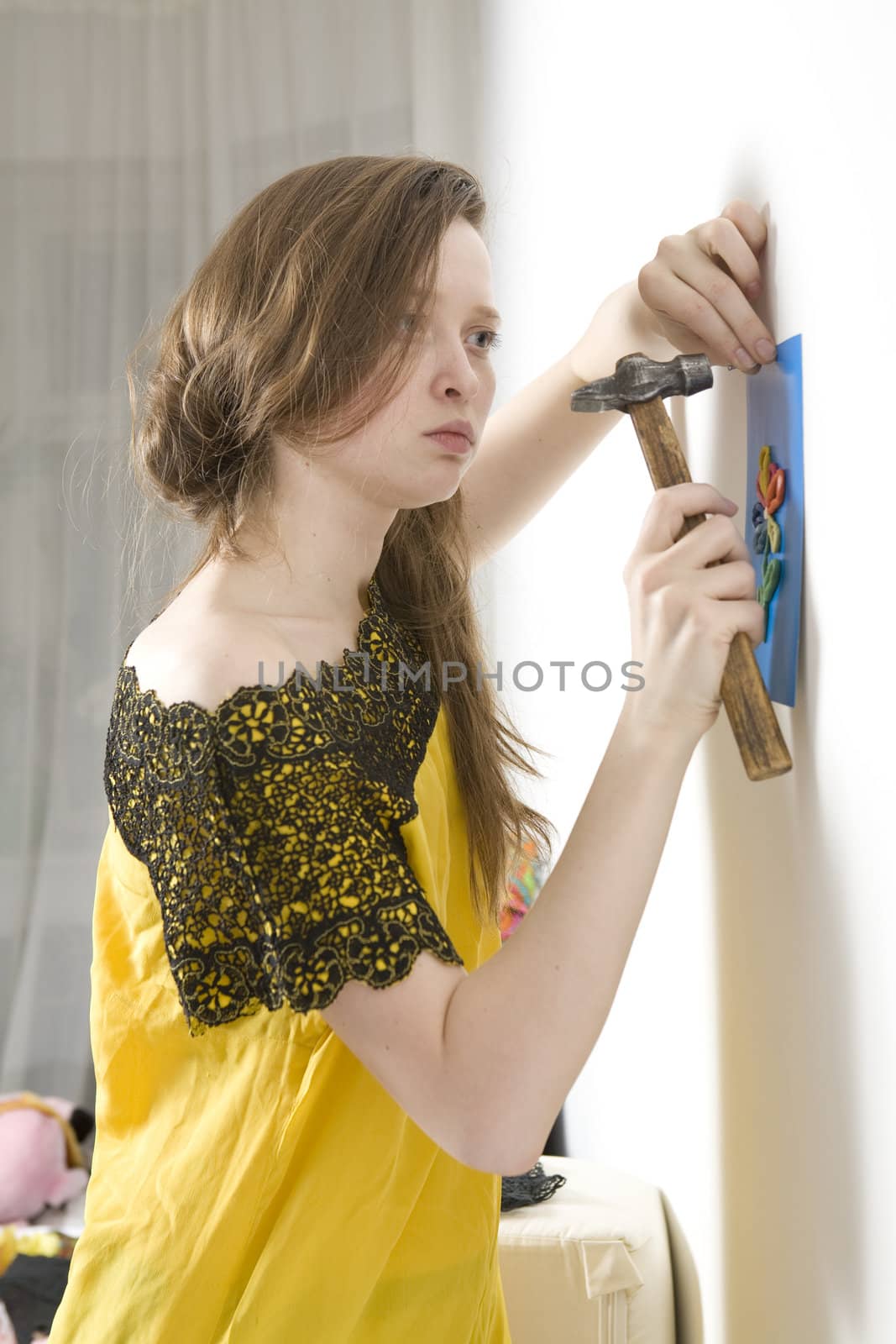 woman in openwork gloves trying to nail picture to white wall. Child picture.