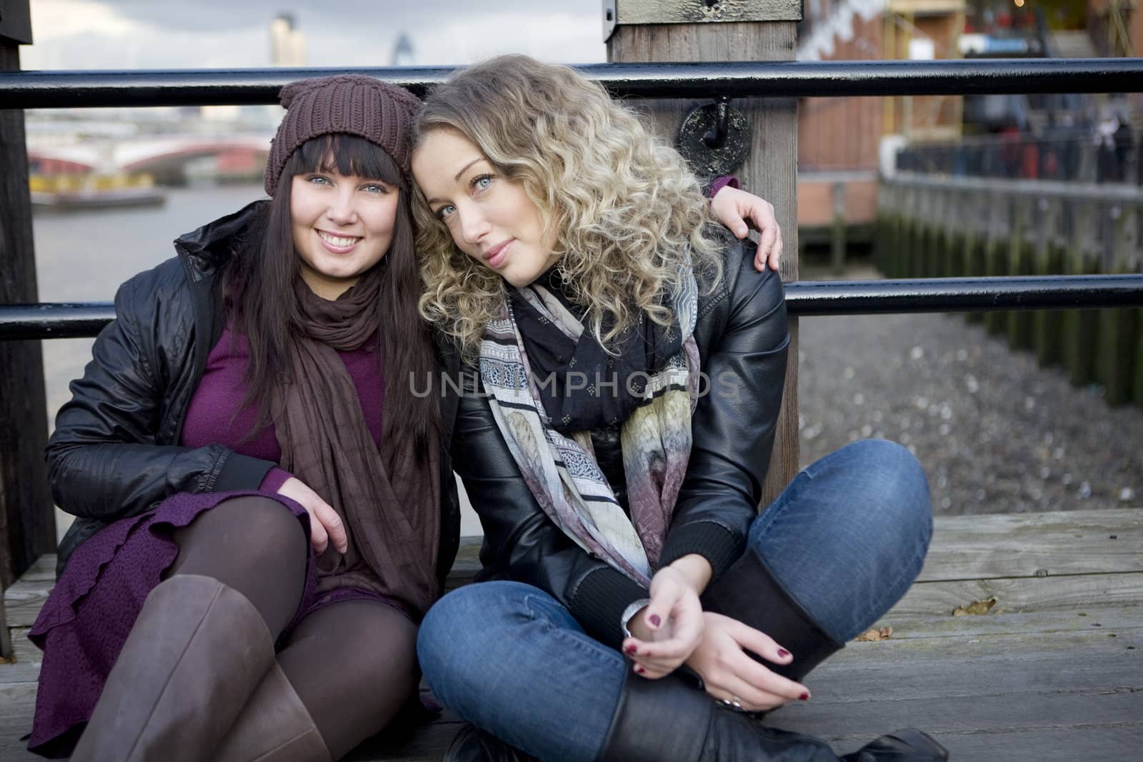 portrait of attractive embracing girls sitting on the bridge. Lo by elenarostunova