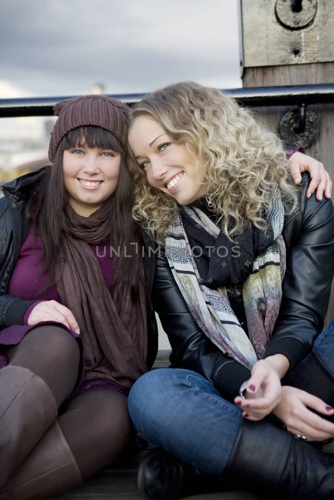 portrait of attractive embracing girls sitting on the bridge. by elenarostunova