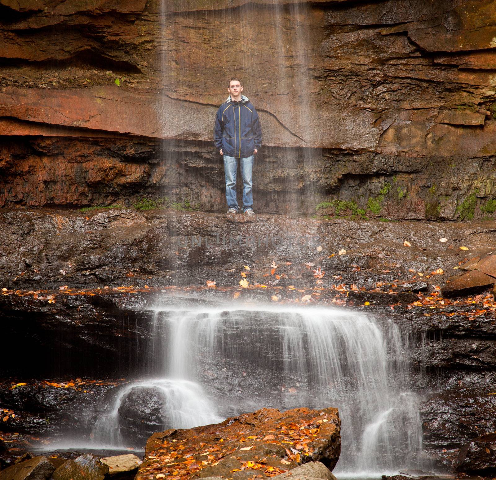 Young man behind the water of Cucumber Falls in Ohiopyle state park in Pennsylvania