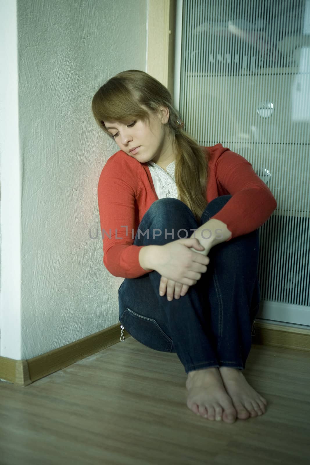 young sad girl sitting on corner in room. Teen`s problem