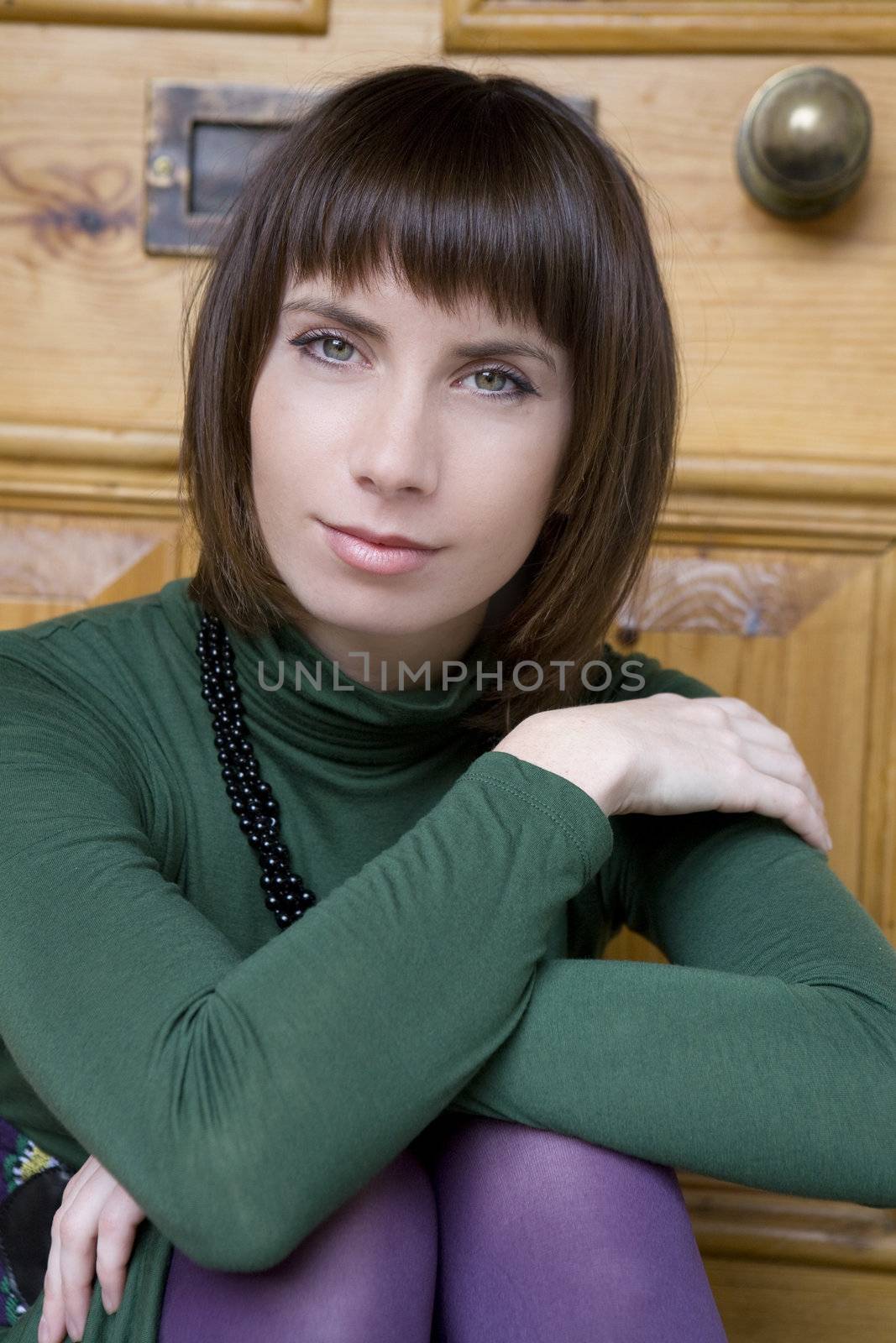 portrait attractive brunette pensive woman with beads wearing green blouse
 at door 
