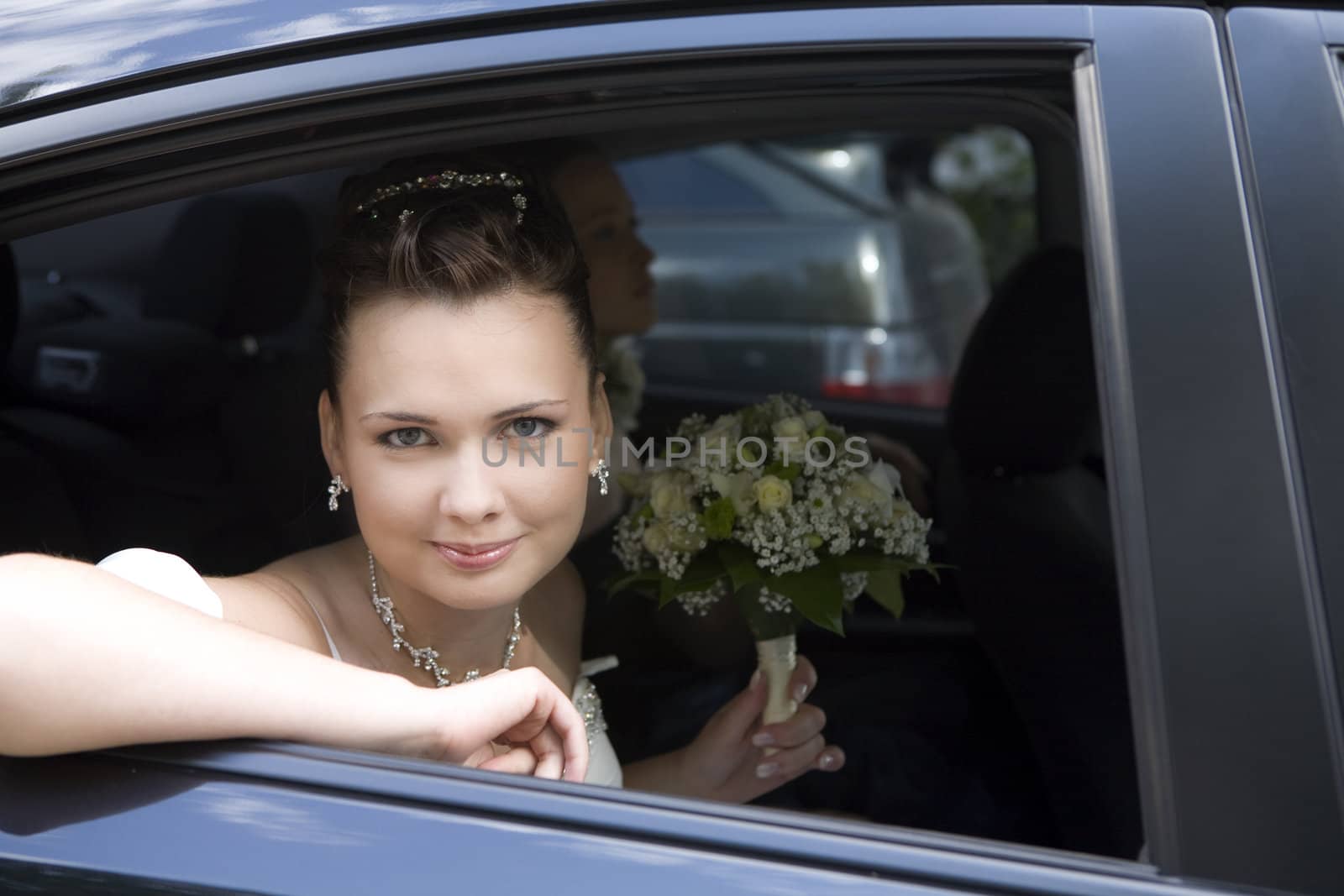 bride with bouquet sitting in wedding car looking through the window