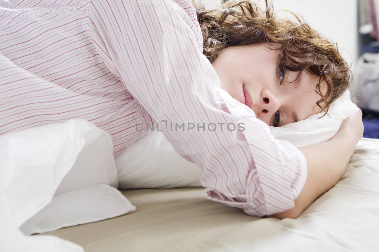 attractive thoughtful brunette curl woman with a pillow on the bed.  Woman`s problem