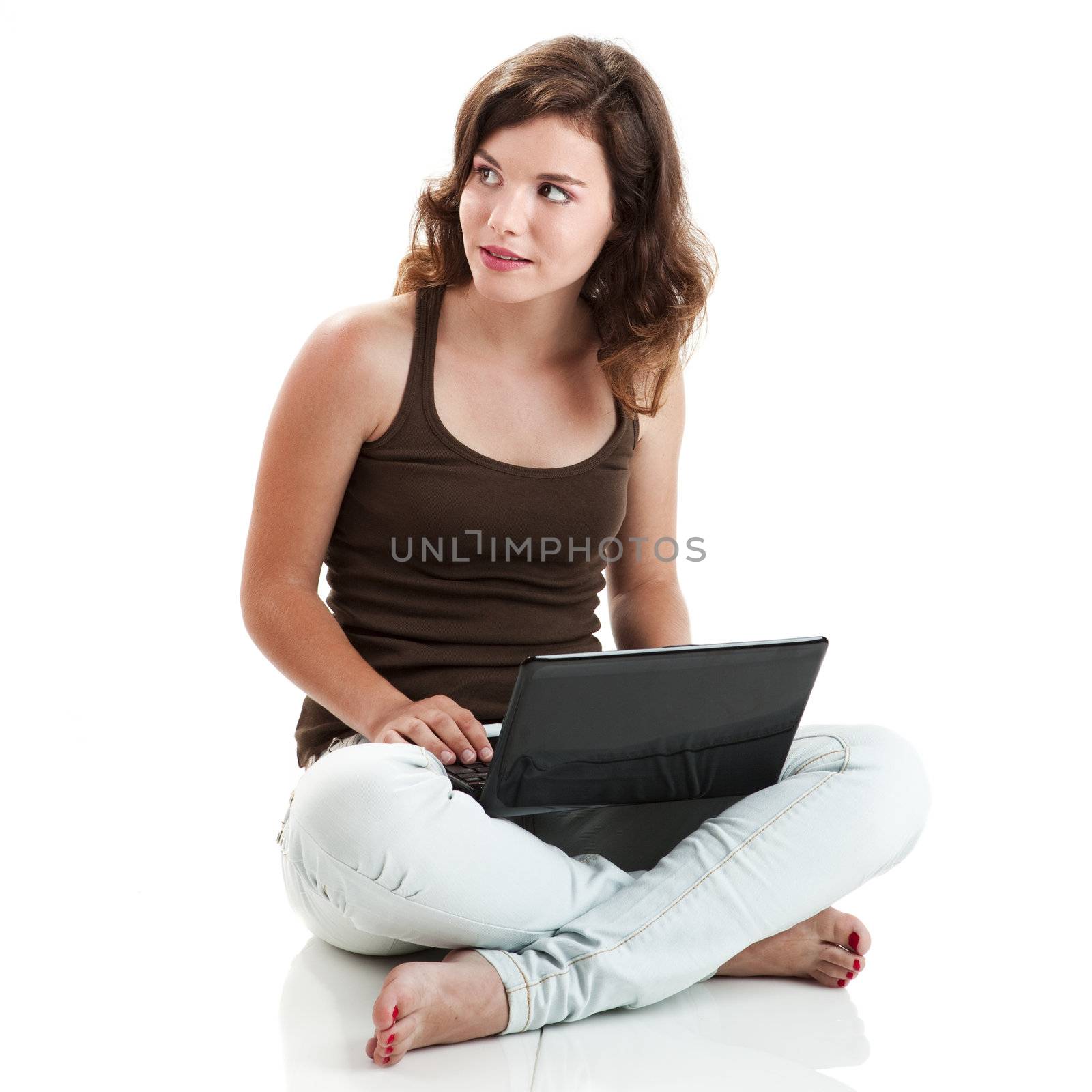 Beautiful young woman sitting on floor with a laptop, isolated on white