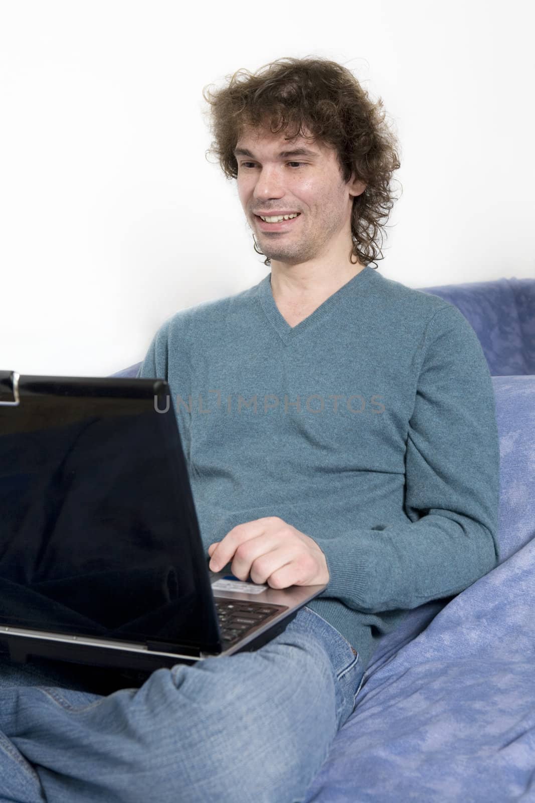Young middle-age  man sitting on the sofa using a laptop compute by elenarostunova