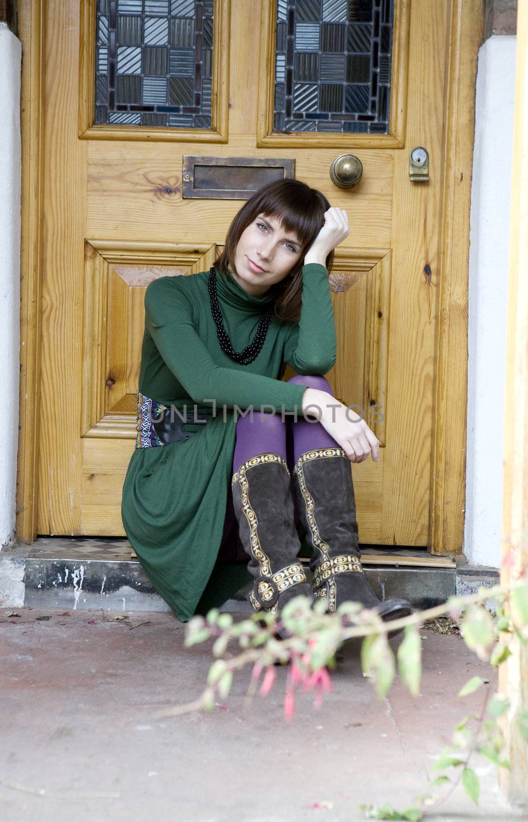 portrait young attractive  woman sitting on doorstep at door wearing green dress and violet stocking