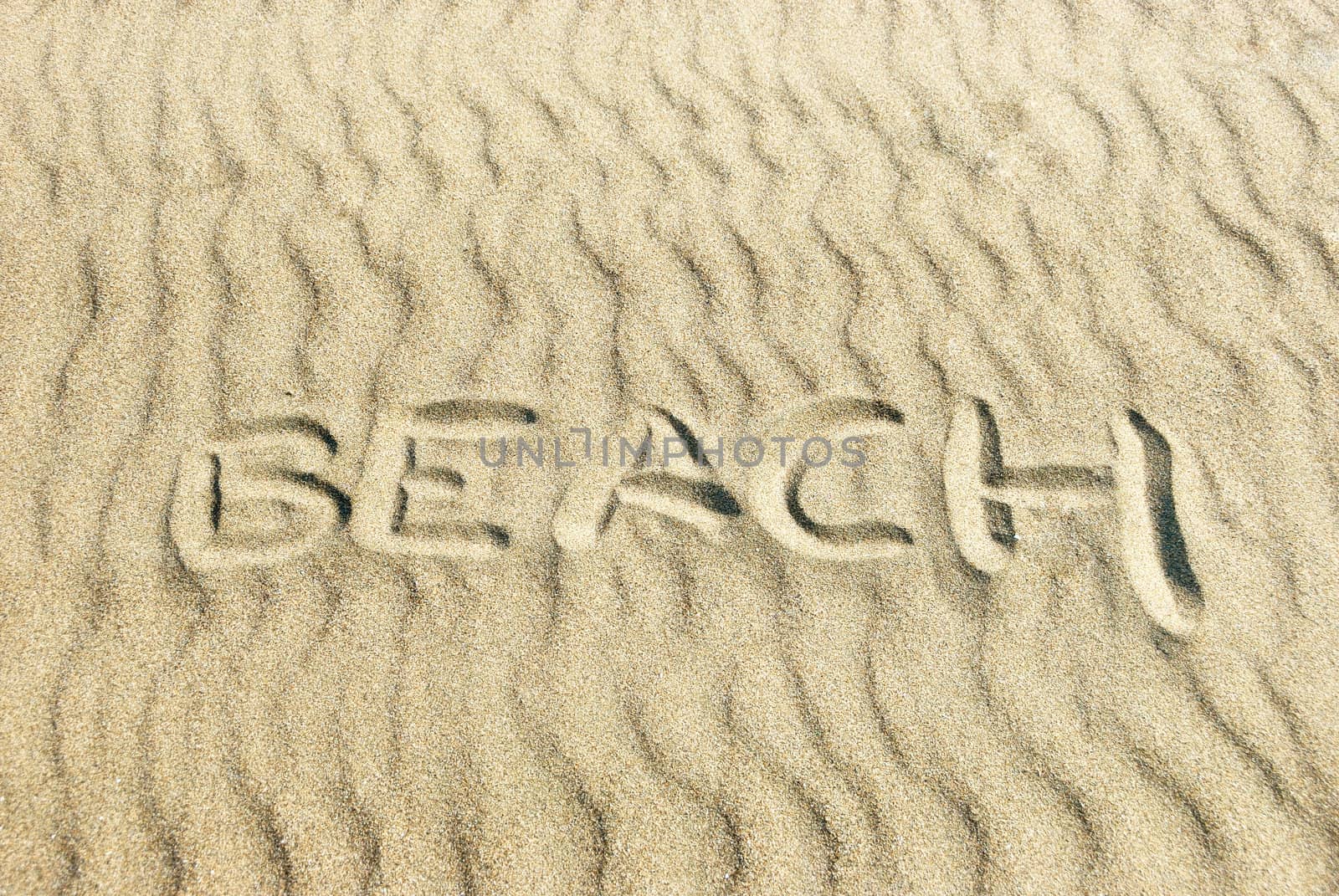 Word BEACH written in sand with sunlight coming from the right.