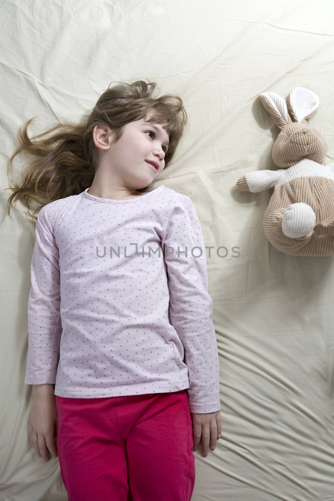 little cute girl lying on bed with hare toy