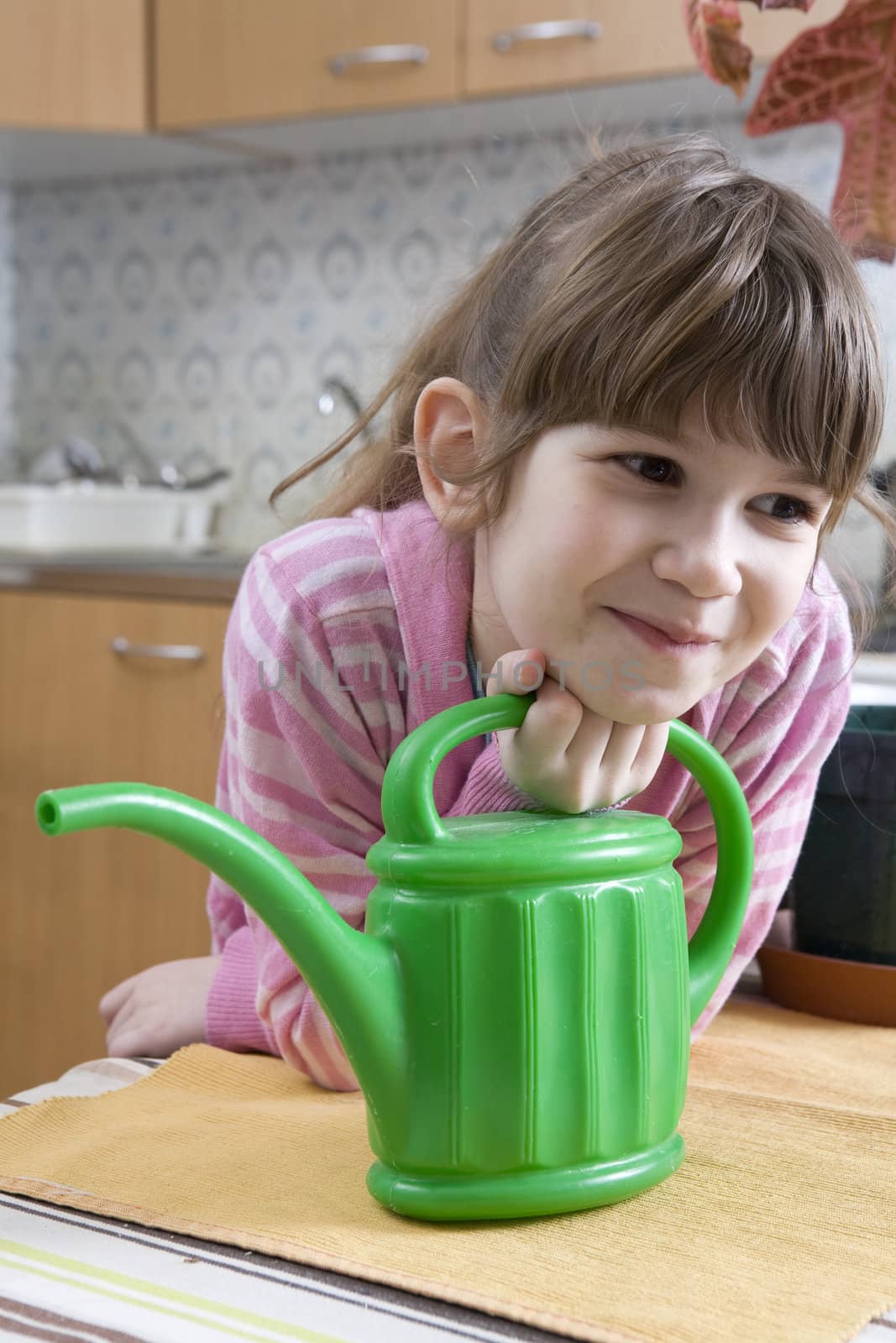 little cute girl seven years old with watering-can sitting on kitchen