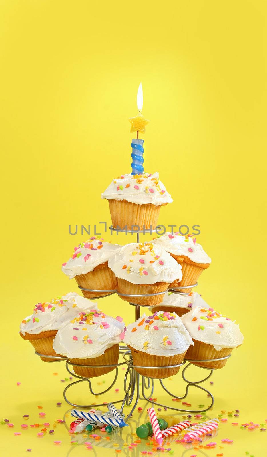 Cupcakes on multi-tiered stand with candle on yellow background