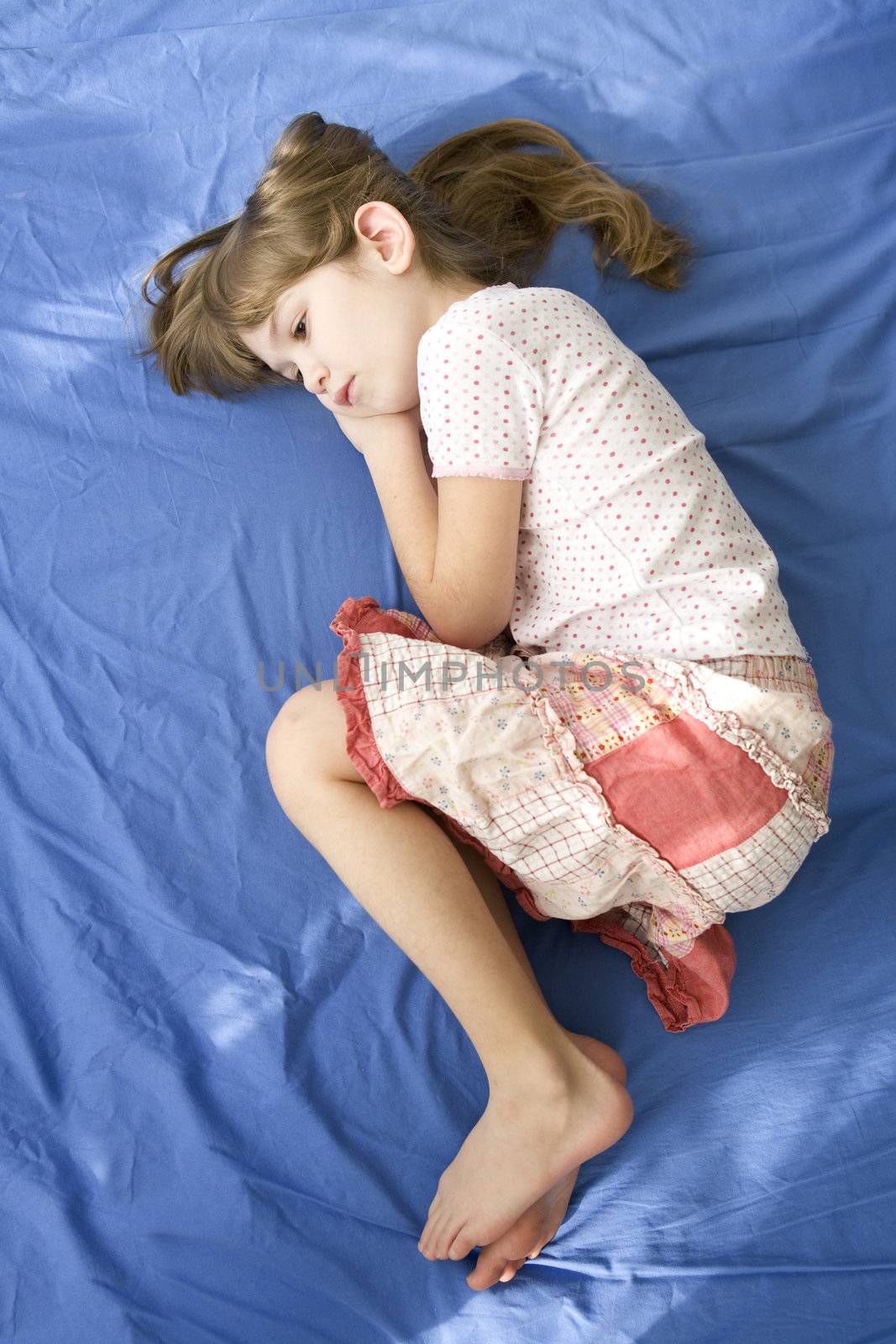 little dreaming girl lying on the bed. Blue cotton sheet by elenarostunova