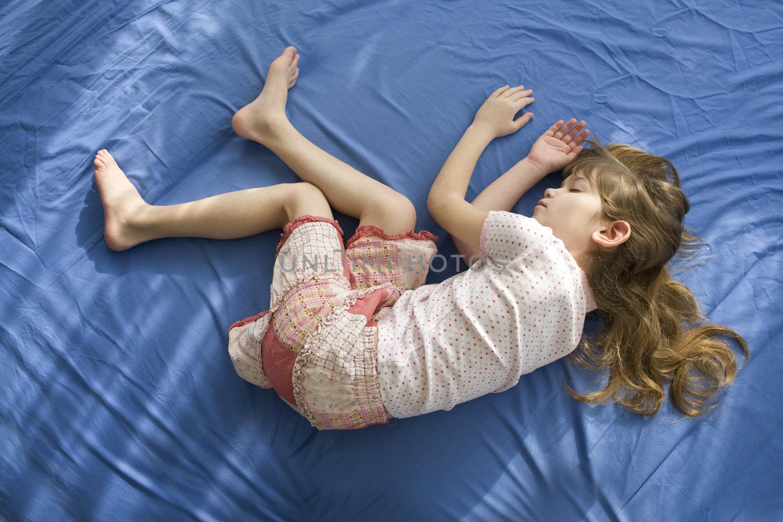little sleeping girl lying on the bed. Blue cotton sheet by elenarostunova